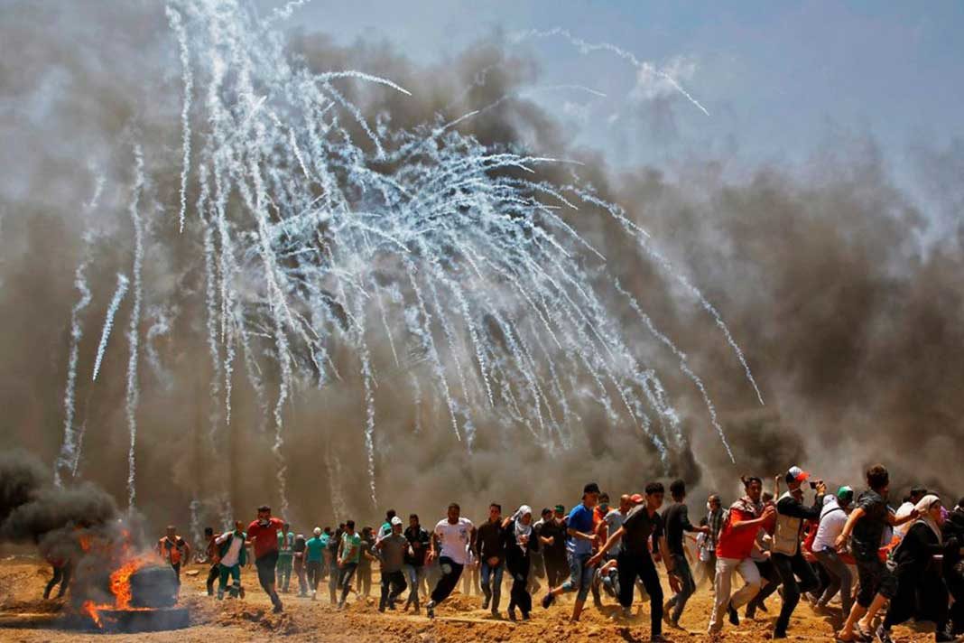 Palestinians run for cover from tear gas during clashes with Israeli security forces near Gaza border