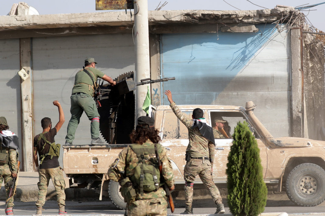 Turkey-backed Syrian fighters gesture as their comrade fires a weapon mounted on a truck in the town of Tell Abyad, Syria, Oct. 13, 2019.