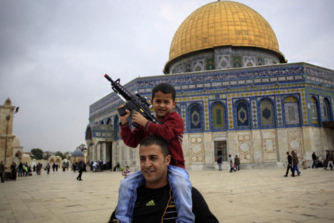 A Palestinian child plays with a toy gun on his father's shoulders at the Al Aqsa Mosque compound in Jerusalem's Old City