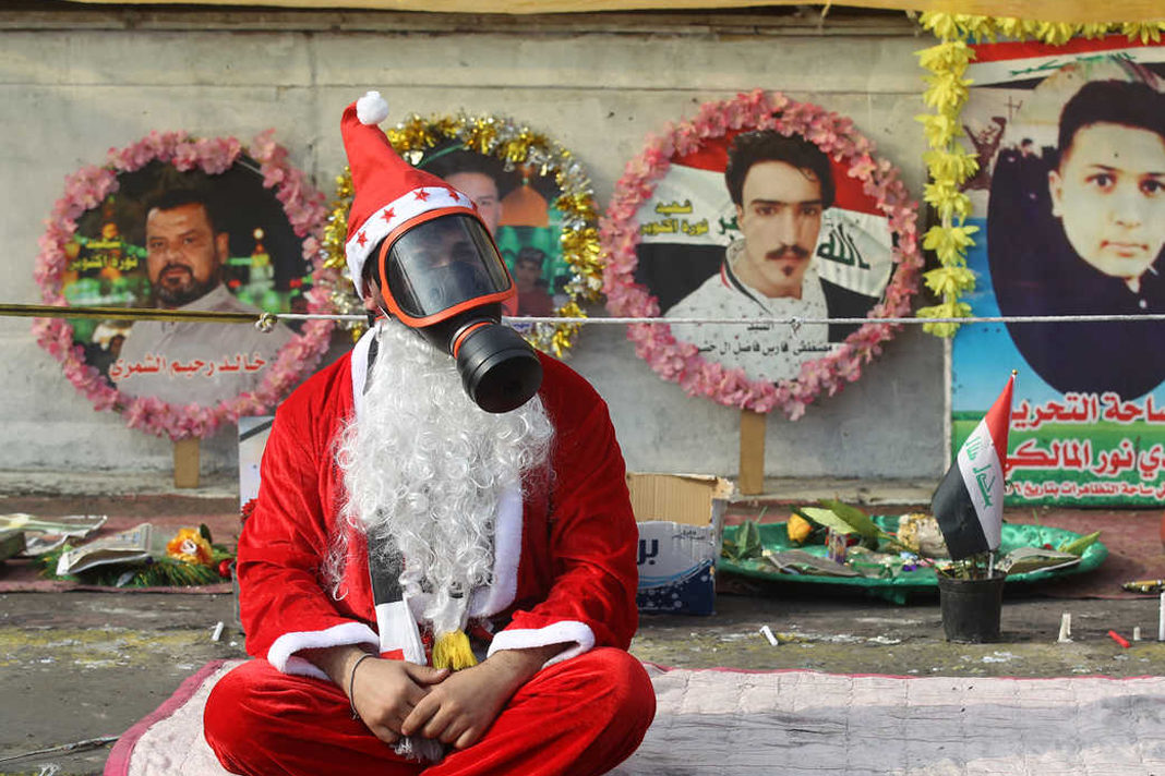 iraq-cancels-christmas An Iraqi demonstrator wearing a Santa Claus costume and a gas mask sits on a blanket in the capital Baghdad's Tahrir Square, amid ongoing anti-government protests