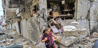 A woman walks among ruins in a village in the Republic of Artsakh bombed by Azerbaijan, October 2020. / Yan Boechat, VOA, Wikimedia Commons.