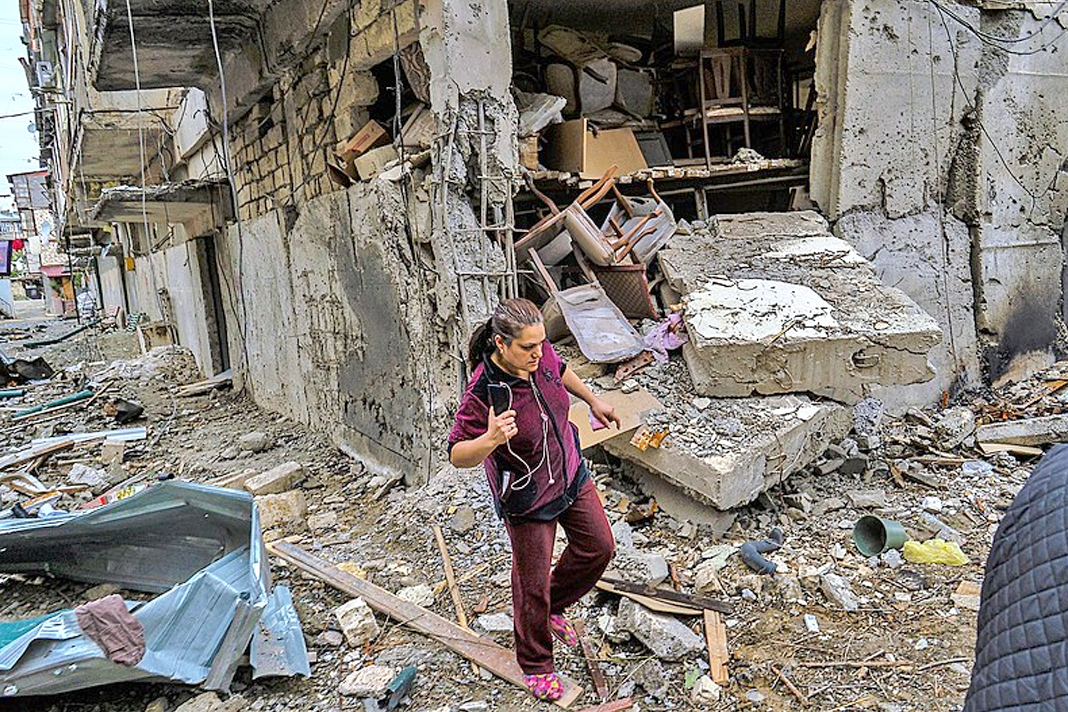 armenians-pray-that-god-will-uphold-the-sovereign-borders-and-end-the-conflict-with-azerbaijan A woman walks among ruins in a village in the Republic of Artsakh bombed by Azerbaijan, October 2020. / Yan Boechat, VOA, Wikimedia Commons.